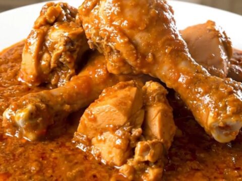 A close-up of a steaming, tender chicken rogan josh dish served on a plain white plate.
