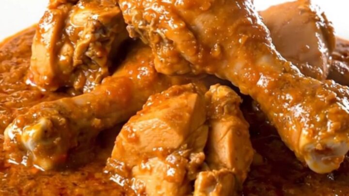 A close-up of a steaming, tender chicken rogan josh dish served on a plain white plate.