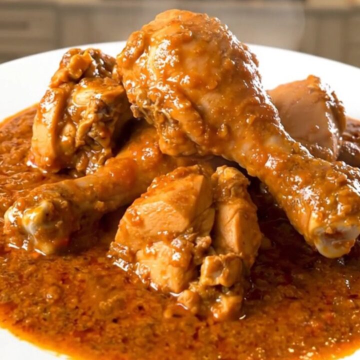 A close-up of a steaming, tender chicken rogan josh dish served on a plain white plate.