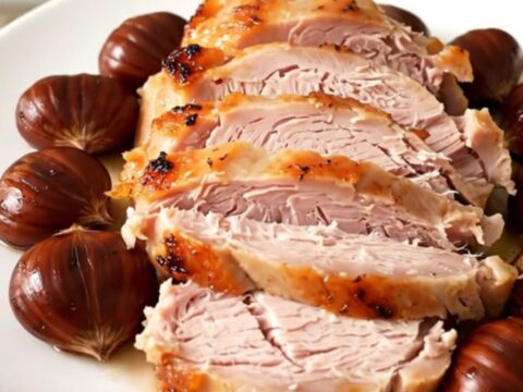 A sliced turkey roast with whole chestnuts on a white plate, steaming and juicy.