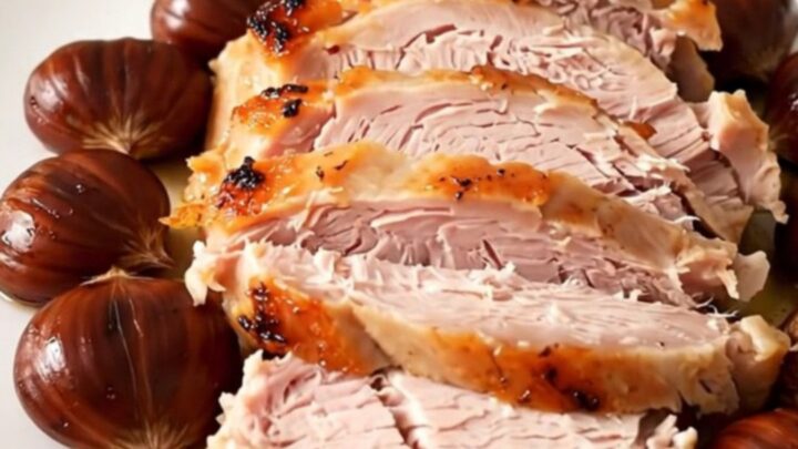 A sliced turkey roast with whole chestnuts on a white plate, steaming and juicy.