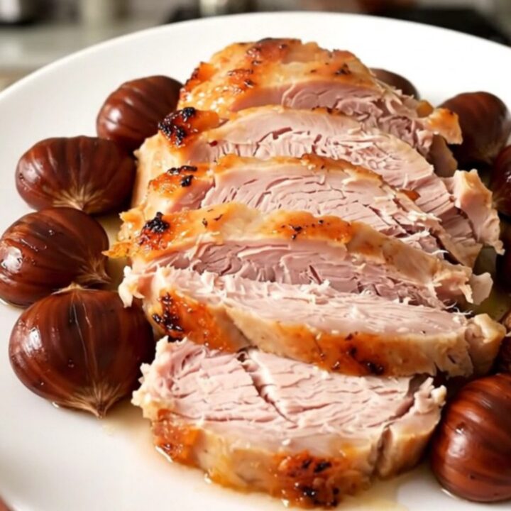A sliced turkey roast with whole chestnuts on a white plate, steaming and juicy.