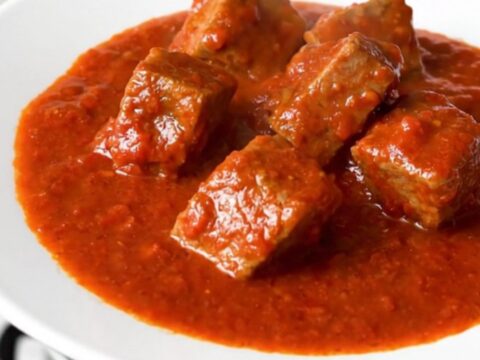 Mijoté de porc au chorizo servi dans une assiette blanche avec une sauce tomate épaisse.