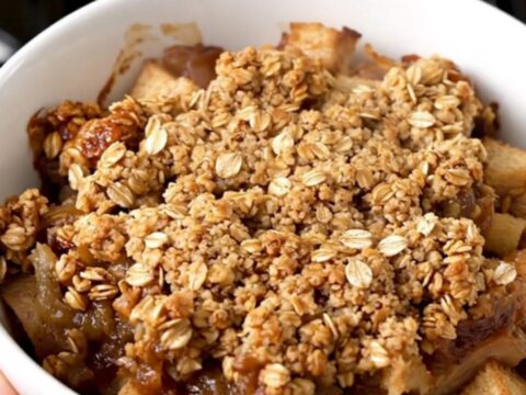 A top-down view of a slow cooker filled with diced apples, oats, cinnamon, and butter cubes ready to cook.