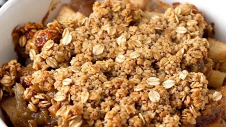 A top-down view of a slow cooker filled with diced apples, oats, cinnamon, and butter cubes ready to cook.