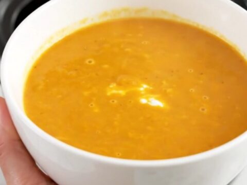 A steaming bowl of smooth, bright orange carrot and sweet potato soup sitting on a clean kitchen counter.