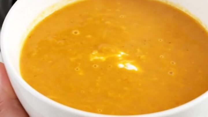 A steaming bowl of smooth, bright orange carrot and sweet potato soup sitting on a clean kitchen counter.