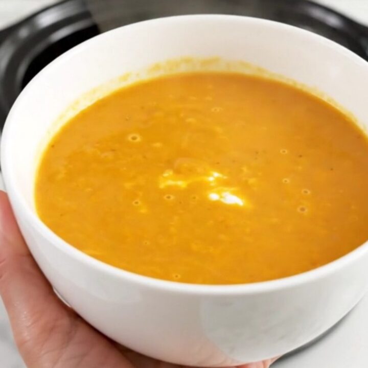 A steaming bowl of smooth, bright orange carrot and sweet potato soup sitting on a clean kitchen counter.