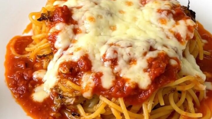 A top-down view of a black slow cooker filled with halved spaghetti squash topped with tomato sauce and herbs.