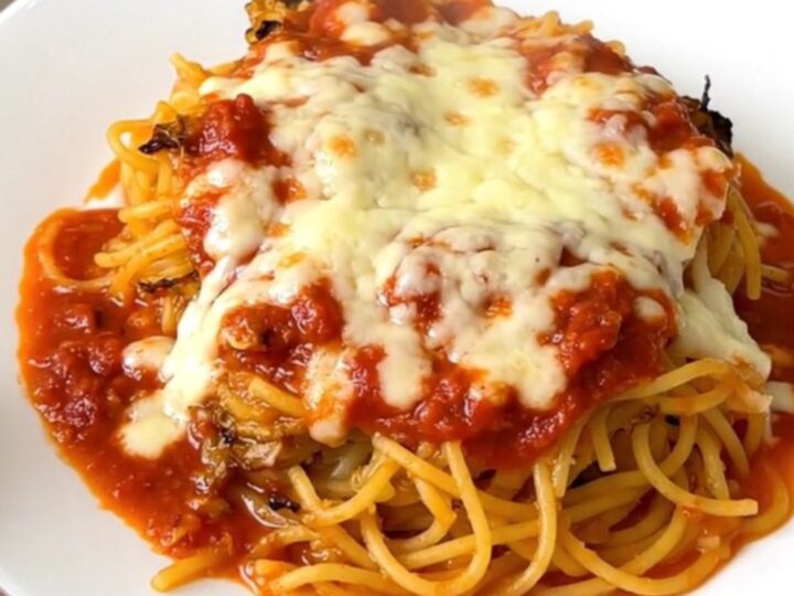 A top-down view of a black slow cooker filled with halved spaghetti squash topped with tomato sauce and herbs.