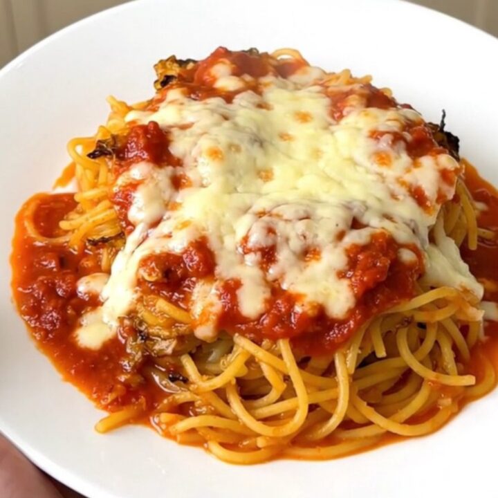 A top-down view of a black slow cooker filled with halved spaghetti squash topped with tomato sauce and herbs.