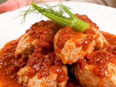 A top-down view of a slow cooker filled with chicken thighs, sliced fennel, and a rich tomato sauce.