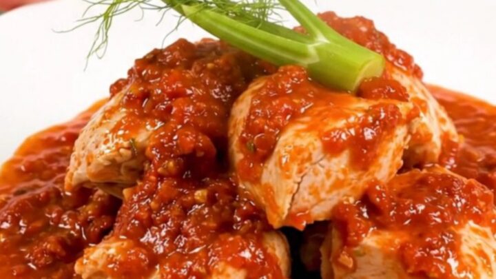 A top-down view of a slow cooker filled with chicken thighs, sliced fennel, and a rich tomato sauce.
