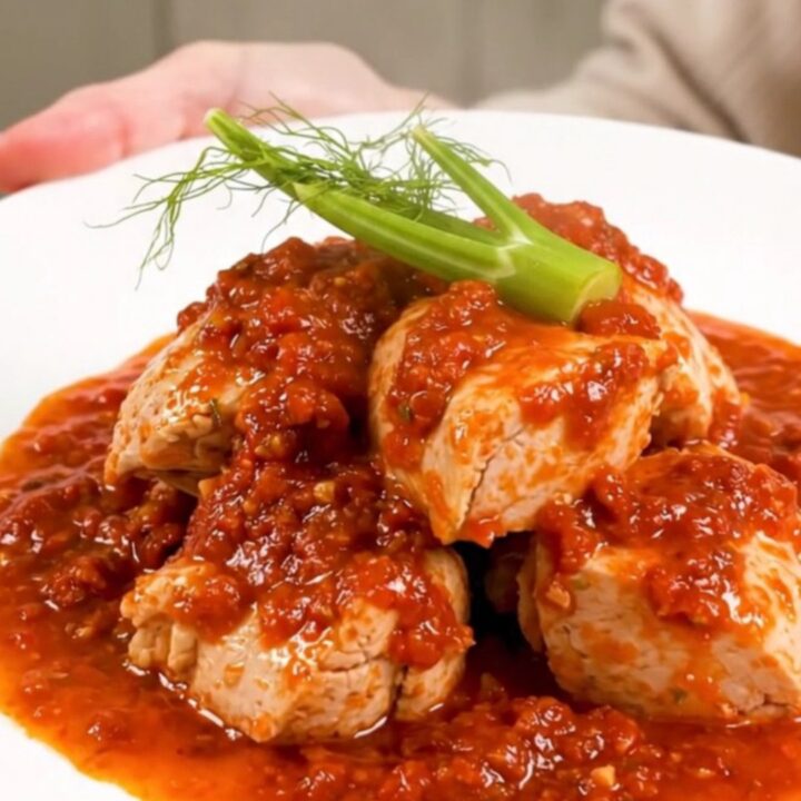 A top-down view of a slow cooker filled with chicken thighs, sliced fennel, and a rich tomato sauce.
