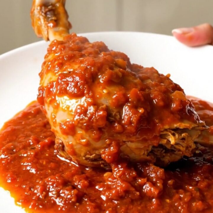 Two tender turkey drumsticks smothered in a rich, glossy tomato oregano sauce on a white plate.