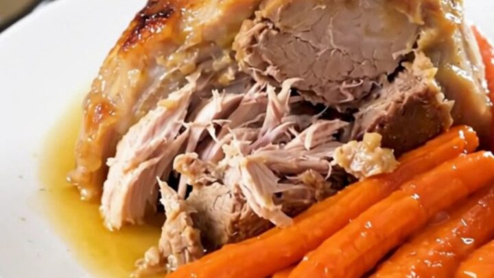 A slow cooker pork roast with sliced carrots and a savory white wine reduction on a white plate.