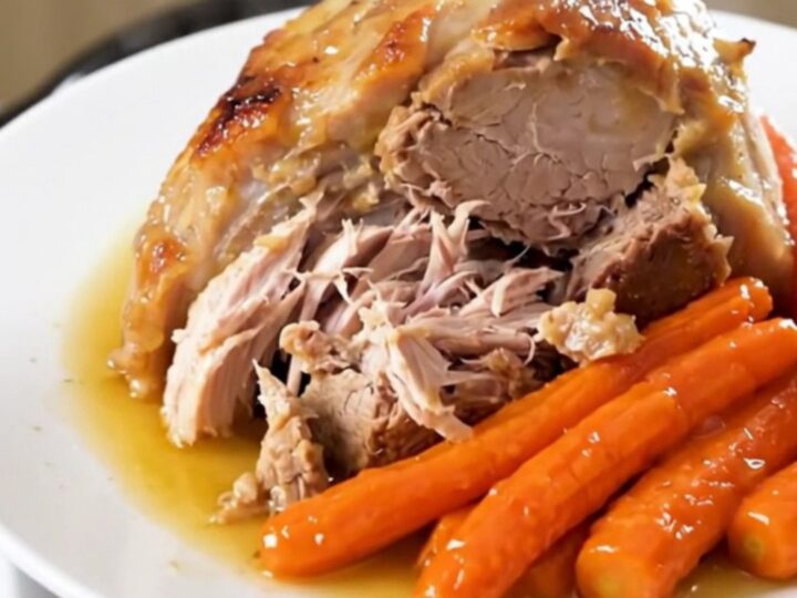 A slow cooker pork roast with sliced carrots and a savory white wine reduction on a white plate.