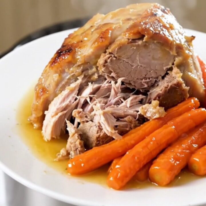 A slow cooker pork roast with sliced carrots and a savory white wine reduction on a white plate.