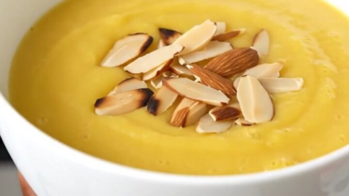 A white ceramic bowl filled with creamy, smooth cauliflower soup garnished with sliced almonds.