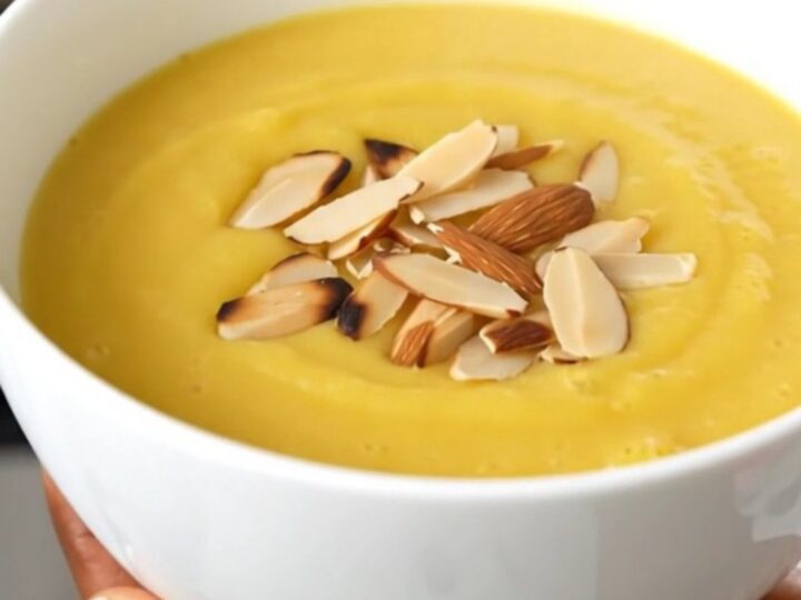 A white ceramic bowl filled with creamy, smooth cauliflower soup garnished with sliced almonds.