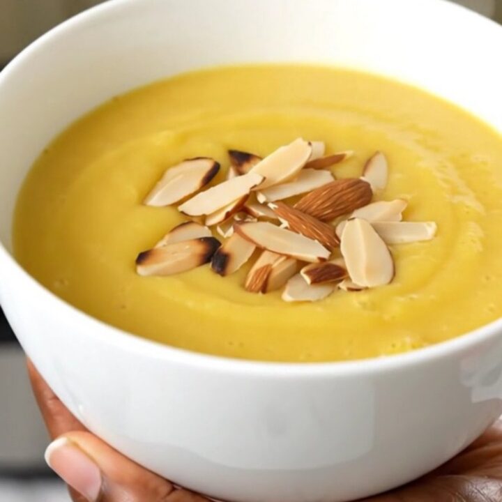 A white ceramic bowl filled with creamy, smooth cauliflower soup garnished with sliced almonds.
