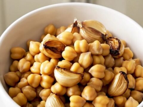 A top-down view of chickpeas, garlic cloves, and fresh thyme sprigs in a slow cooker, ready to be covered in olive oil.