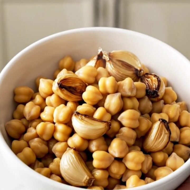 A top-down view of chickpeas, garlic cloves, and fresh thyme sprigs in a slow cooker, ready to be covered in olive oil.