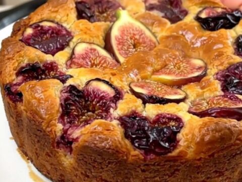 A warm, golden-brown fig and almond clafoutis served on a white plate with visible pieces of fresh fig.