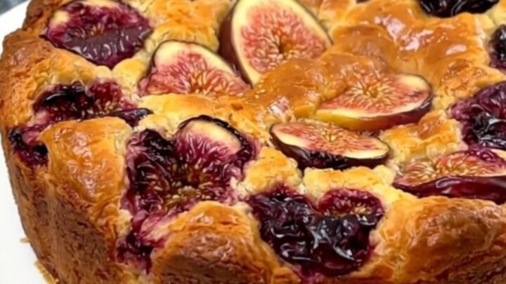 A warm, golden-brown fig and almond clafoutis served on a white plate with visible pieces of fresh fig.