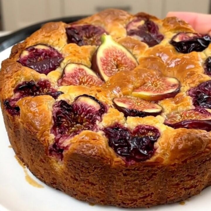 A warm, golden-brown fig and almond clafoutis served on a white plate with visible pieces of fresh fig.