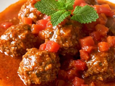 Steaming slow cooker beef meatball tagine coated in glossy tomato sauce with cumin and dried mint.