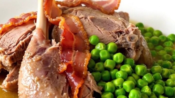 A rustic slow-cooked guinea fowl dish with bacon lardons and bright green peas in a dark oval slow cooker.
