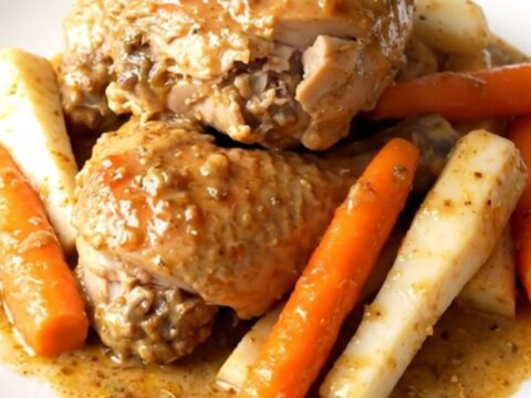 Close-up of creamy slow cooker chicken with sliced carrots and parsnips served on a white plate.