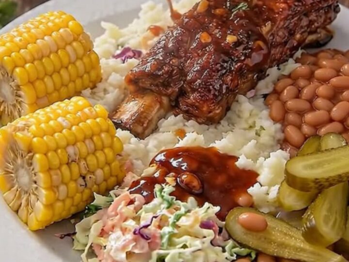 Sticky garlic BBQ ribs glistening under warm light on a rustic wooden board with side dishes.