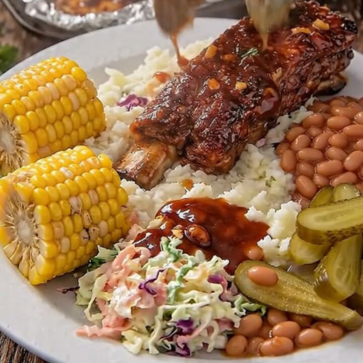 Sticky garlic BBQ ribs glistening under warm light on a rustic wooden board with side dishes.