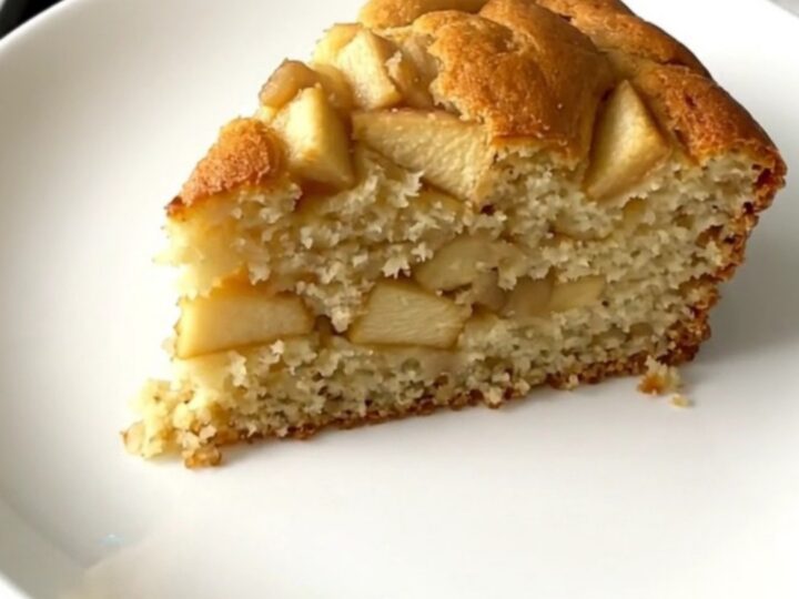 A golden, moist slice of apple yogurt cake served on a simple white plate.