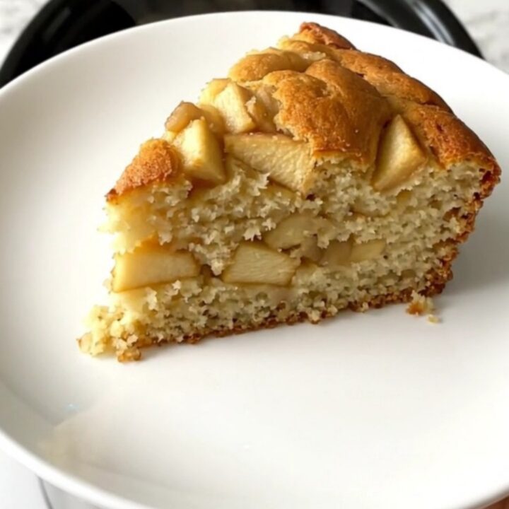 A golden, moist slice of apple yogurt cake served on a simple white plate.
