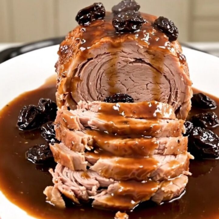A beautifully plated slow cooker pork roast sliced to show tender meat, garnished with prunes and bacon.