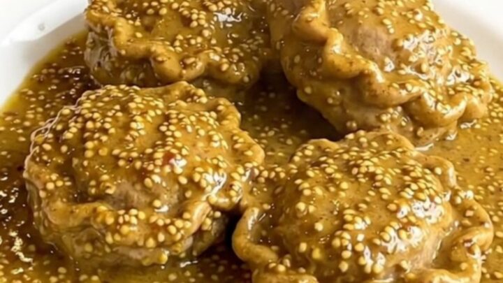 A close-up of tender veal paupiettes coated in a creamy, glossy mustard sauce on a white plate.
