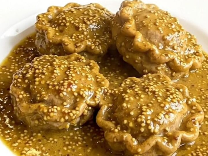 A close-up of tender veal paupiettes coated in a creamy, glossy mustard sauce on a white plate.