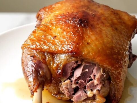 A close-up of crispy, golden-brown duck confit with fresh rosemary on a white plate.