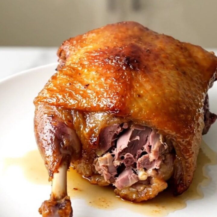 A close-up of crispy, golden-brown duck confit with fresh rosemary on a white plate.