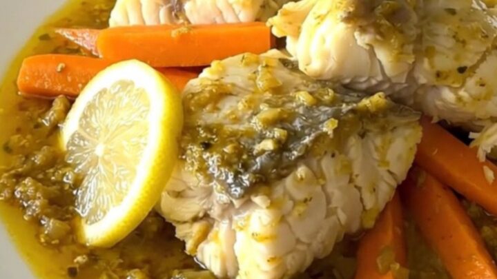 A close-up of a slow cooker filled with white fish, carrot sticks, and lemon slices ready to be cooked.