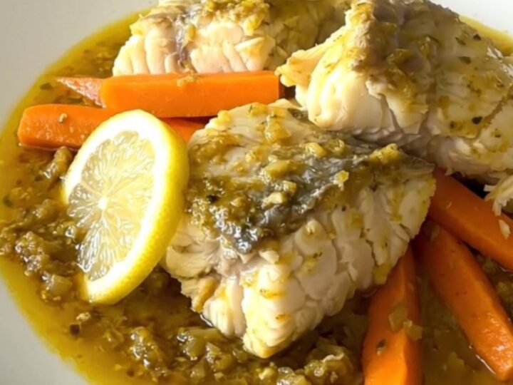 A close-up of a slow cooker filled with white fish, carrot sticks, and lemon slices ready to be cooked.