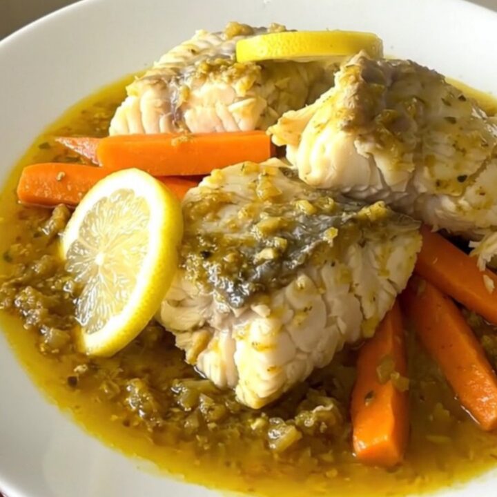 A close-up of a slow cooker filled with white fish, carrot sticks, and lemon slices ready to be cooked.