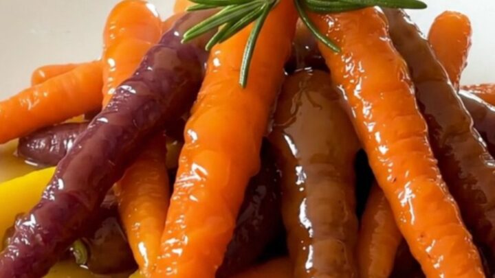 A top-down view of glazed heirloom carrots in a slow cooker with rosemary and orange zest.