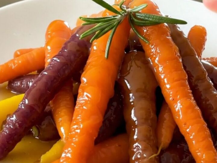 A top-down view of glazed heirloom carrots in a slow cooker with rosemary and orange zest.