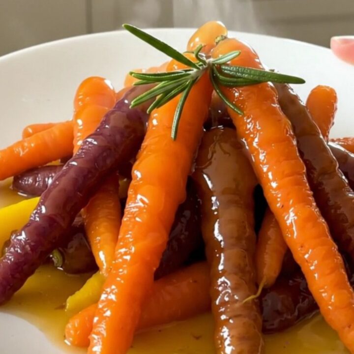 A top-down view of glazed heirloom carrots in a slow cooker with rosemary and orange zest.