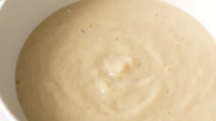 A steaming, glossy white bowl of turnip and leek cream soup set against a soft-blurred cream kitchen background.