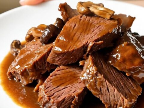 A close-up of tender braised beef and porcini mushrooms served on a white plate.